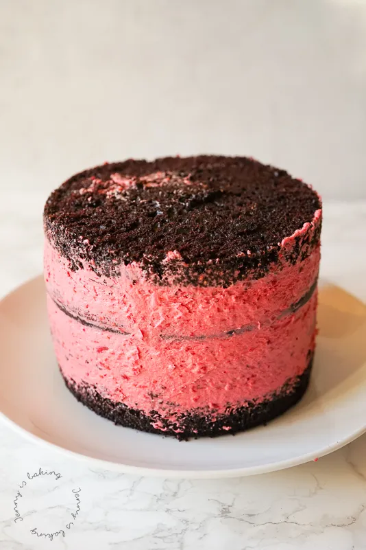 Eine Herztorte, die aus einer runden Backform geschnitten wurde, mit Himbeeren und Schokodrip verziert