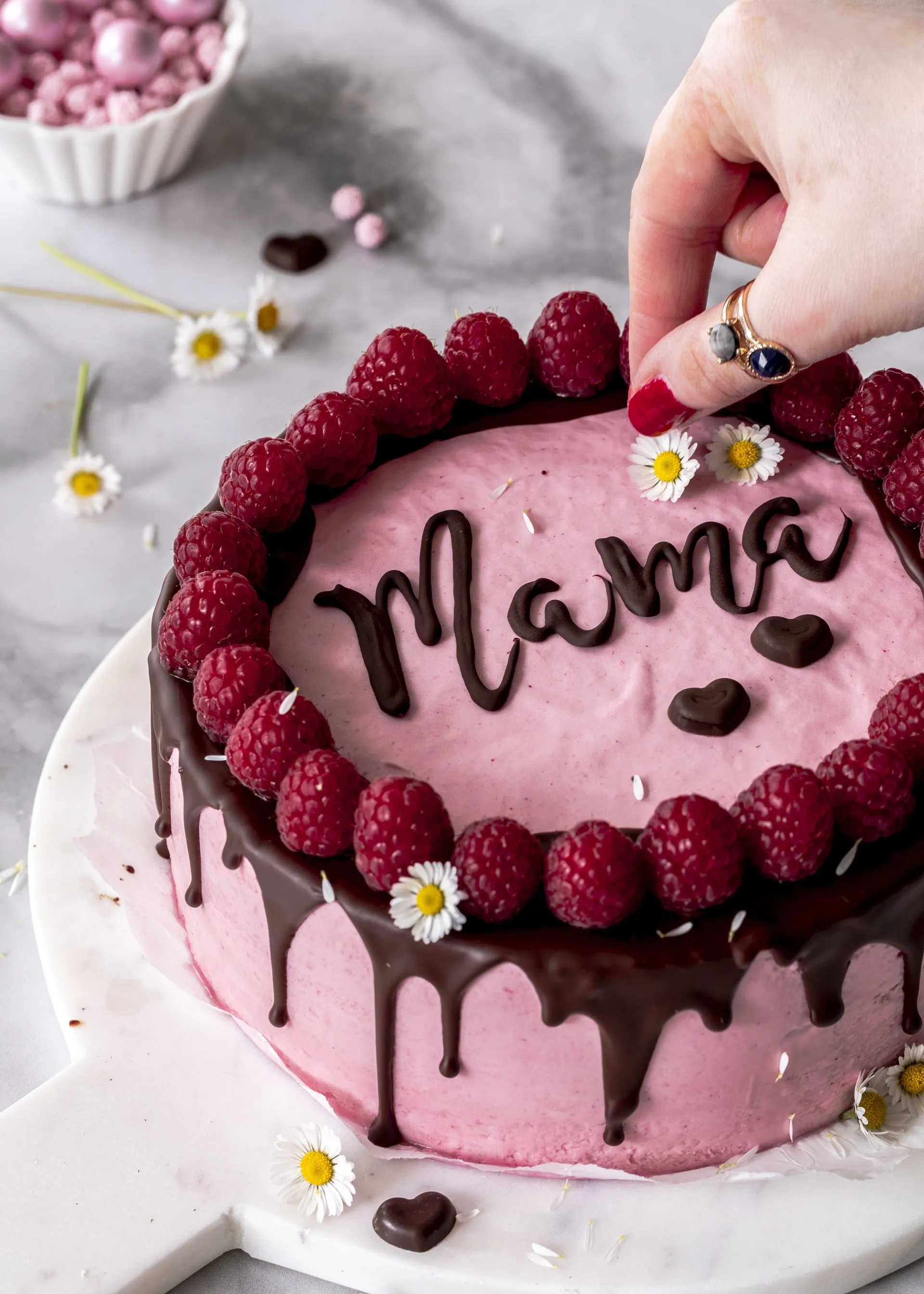 Eine Himbeermousse-Torte mit Schokolade, verziert mit einem Schriftzug "Muttertag" und frischen Himbeeren