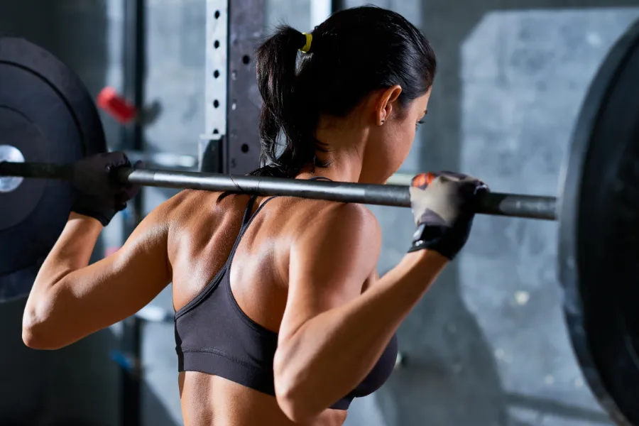 Eine junge Frau trainiert mit Hanteln im Fitnessstudio und lächelt dabei