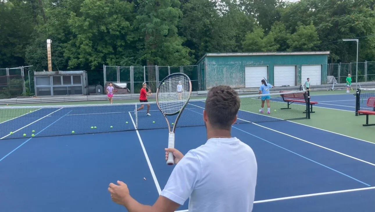 Eine Person in einem weißen Hemd hält einen Tennisschläger und beobachtet Spieler