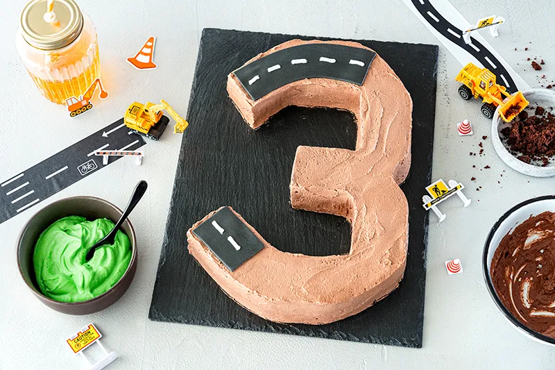 Eine Zahlentorte wird mit Schoko-Creme bestrichen und Fondant-Streifen belegt