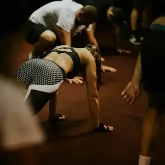 Fitnessgruppe bei funktionellem Workout – Frau in Plank-Position auf Fitnessmatte trainiert Rumpf und Schultern