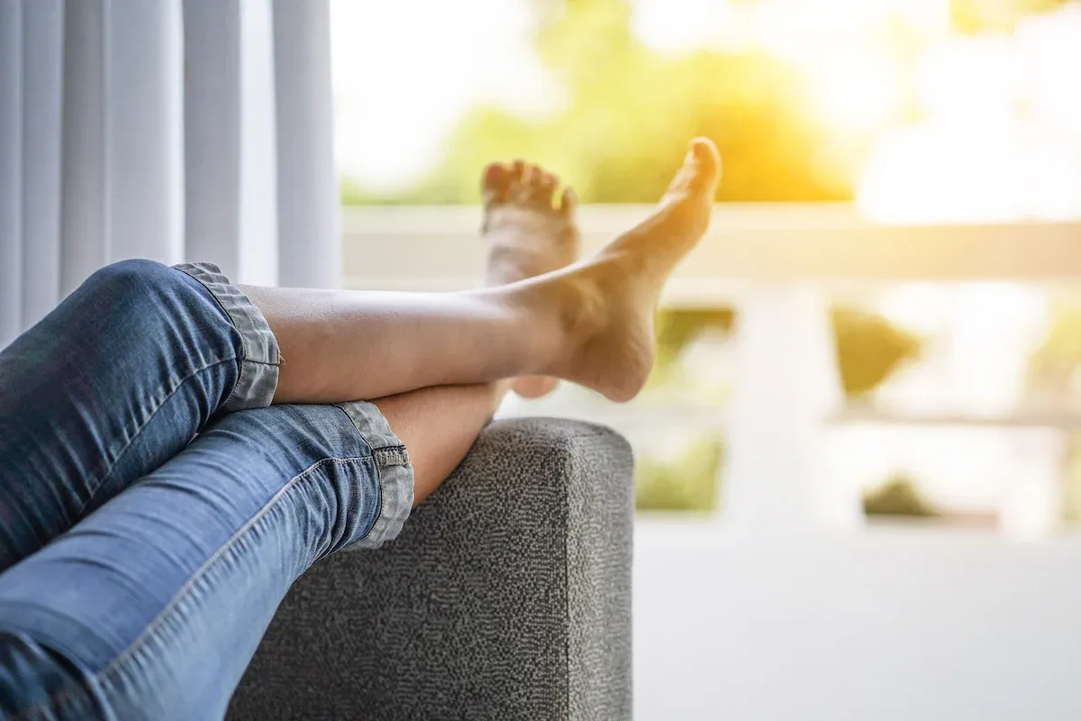 Frau liegt auf dem Sofa und lagert die Beine hoch