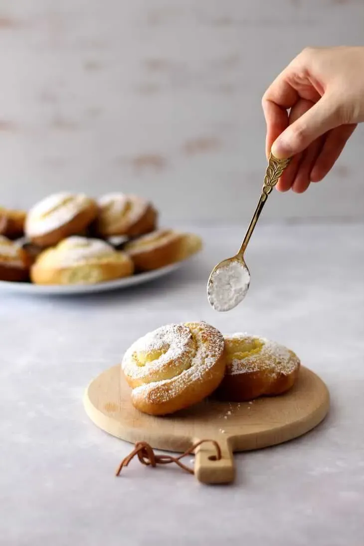 Frisch gebackene Puddingschnecken mit Puderzucker bestreut, auf einem Holztisch präsentiert