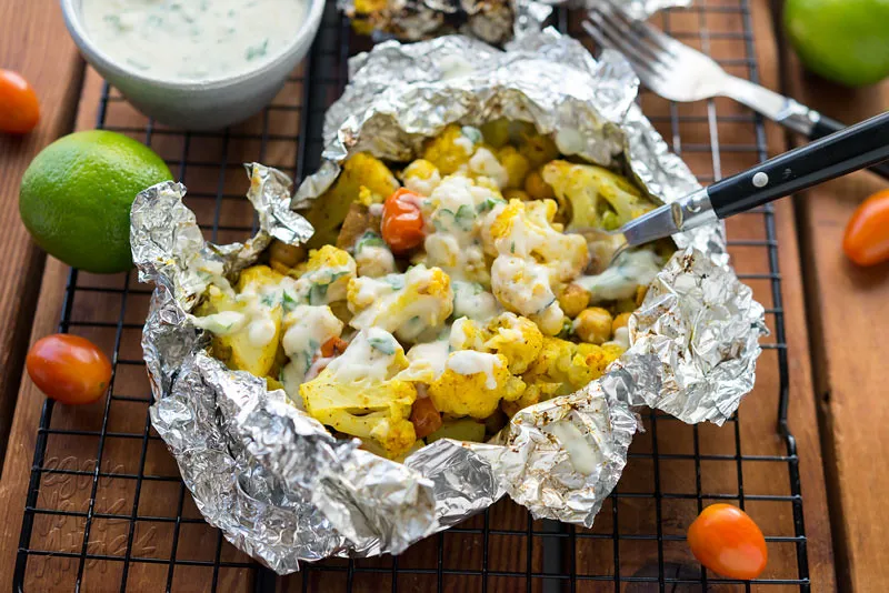 Grillpäckchen gefüllt mit Curry-Blumenkohl-Gemüsemischung, garniert mit Joghurtsauce