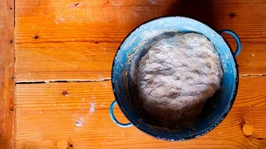 Hefeteig liegt in einer Emailleschüssel auf einem Knetbrett aus Holz.