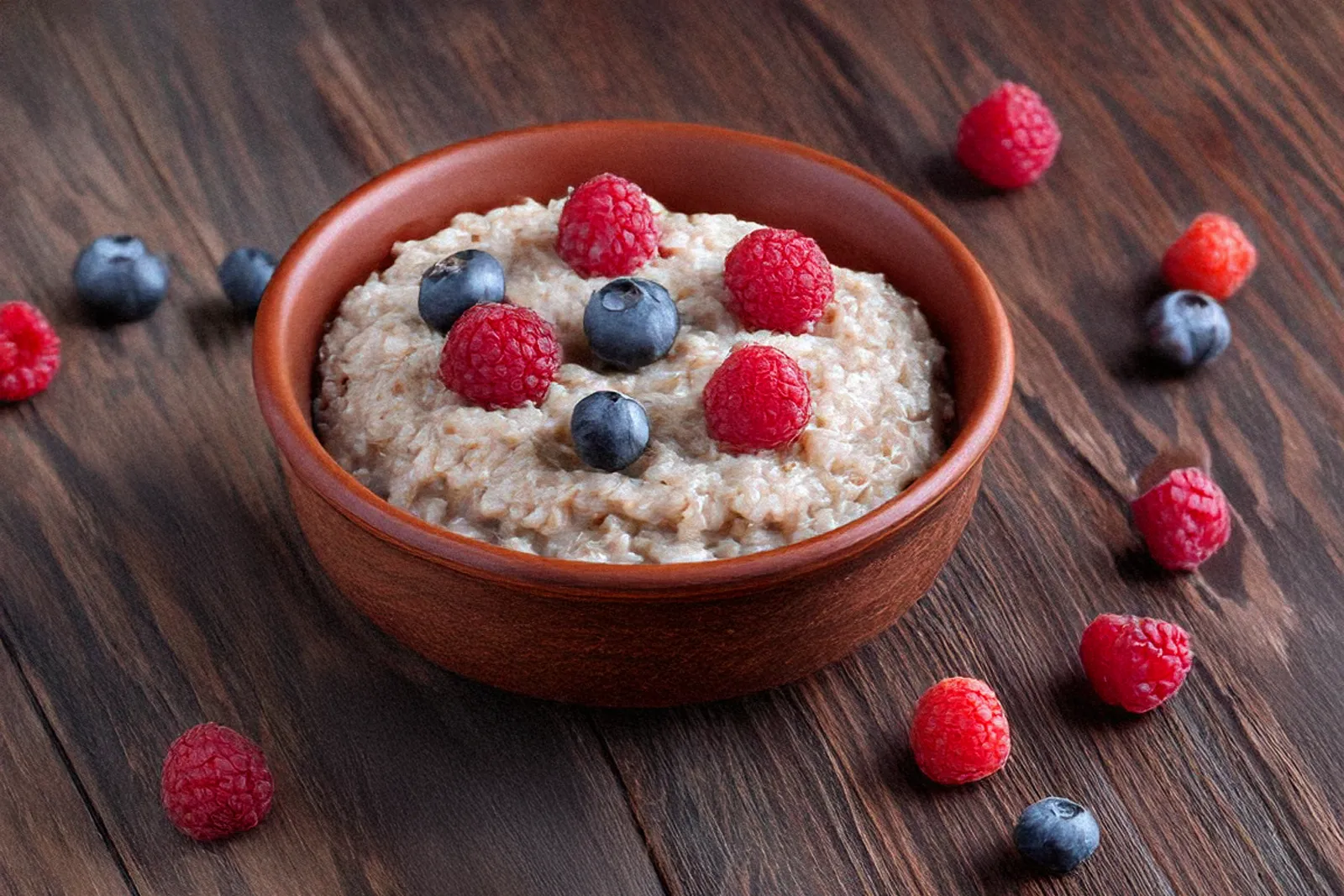 Holzschale mit cremigem Low-Carb-Porridge, garniert mit frischen Himbeeren und Blaubeeren