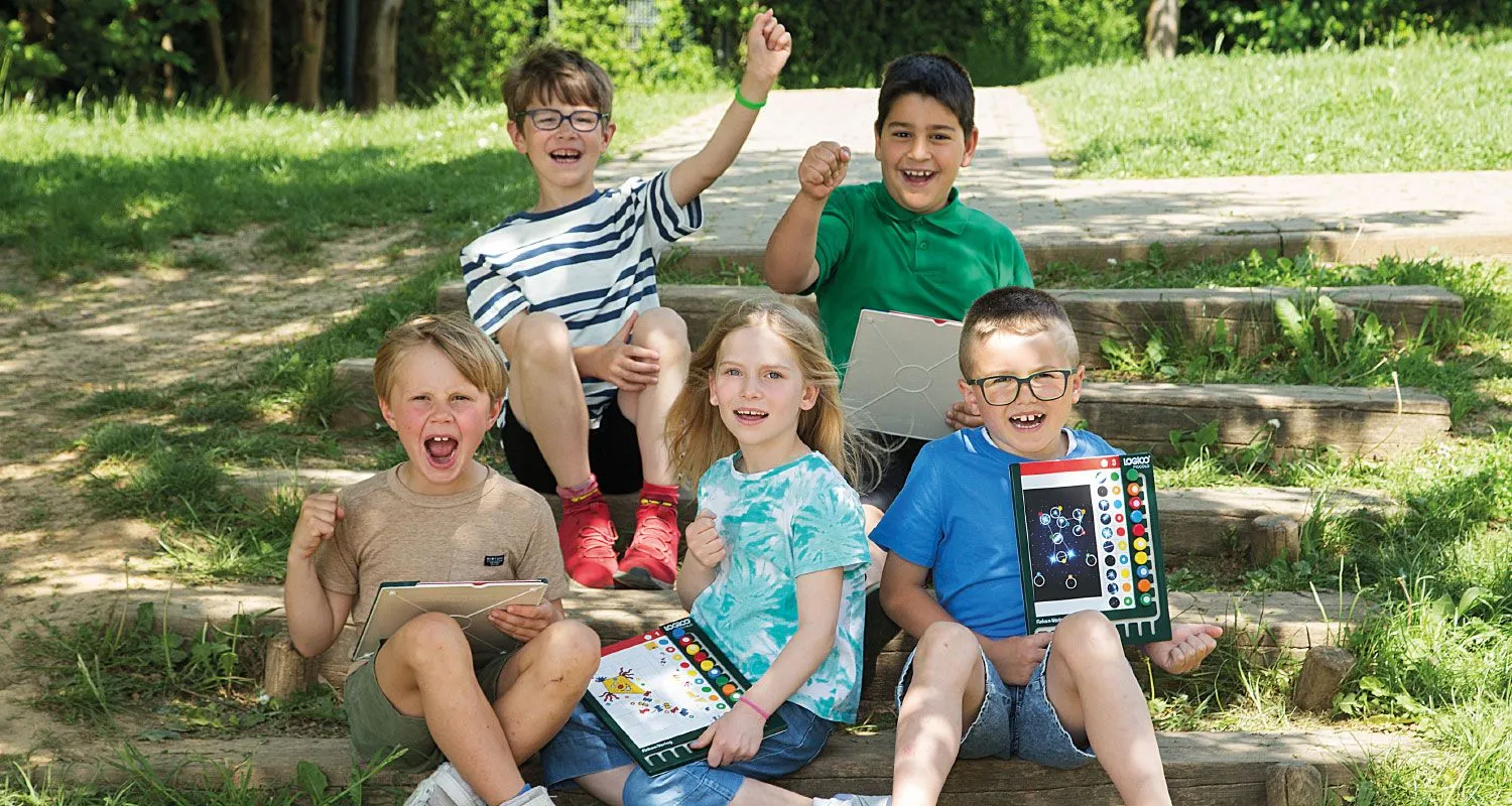 Jubelnde Kinder sitzen draußen auf einer Treppe auf dem Schulgelände und lernen mit LOGICO