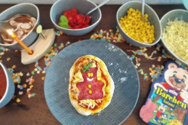 Kinder belegen ihre eigenen kleinen Pizzen auf einem Buffet