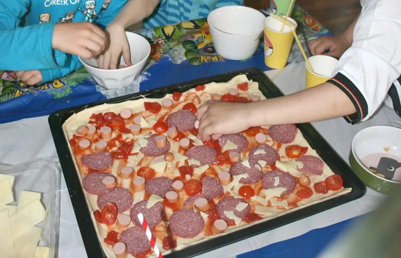 Kinder belegen ihre selbstgemachte Pizza auf einem großen Backblech während der Pokémon Mottoparty