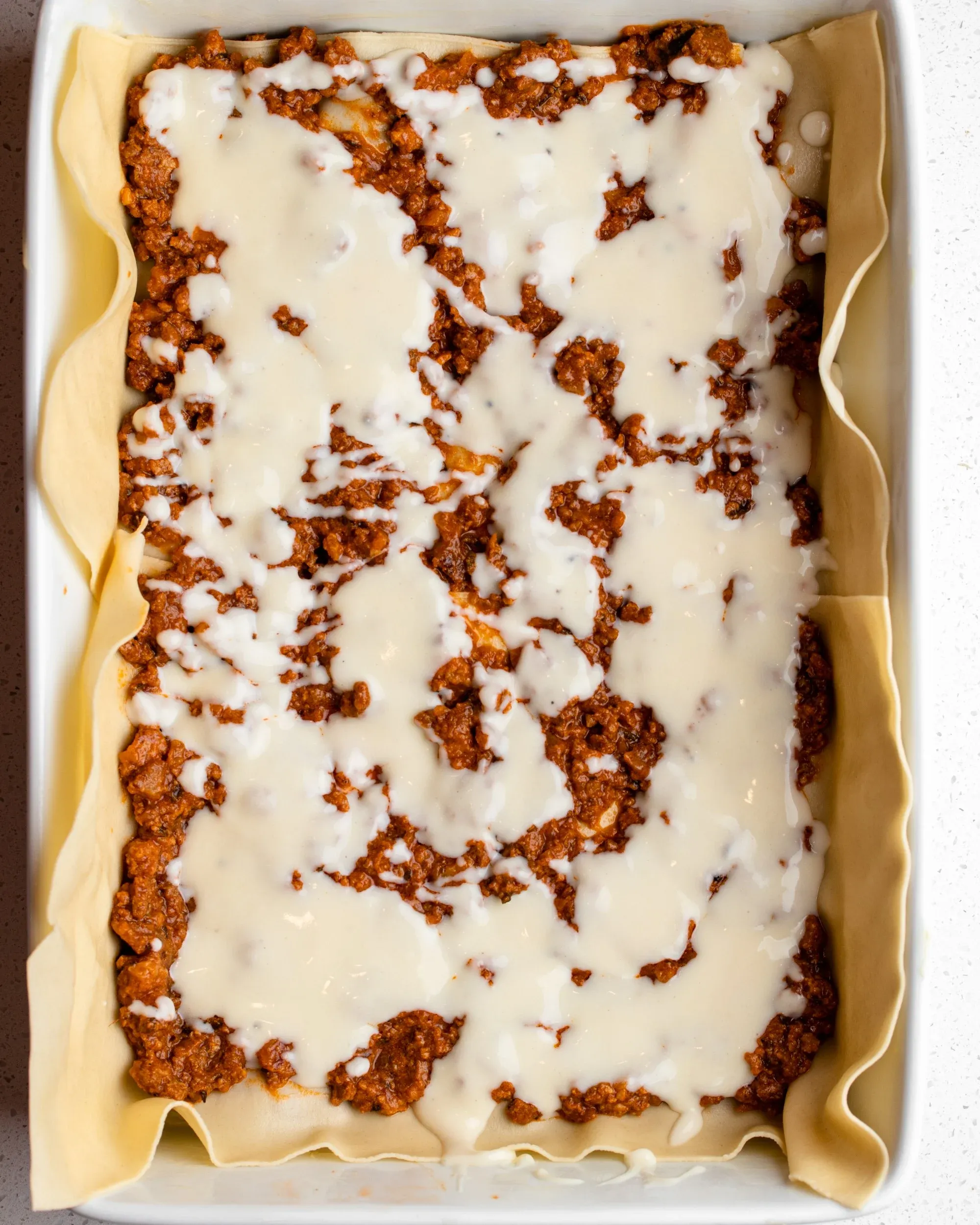 Lasagne wird weiter geschichtet. Béchamelschicht über dem Fleisch.