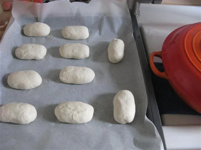 Mehrere längliche Brötchenteiglinge auf dem Blech
