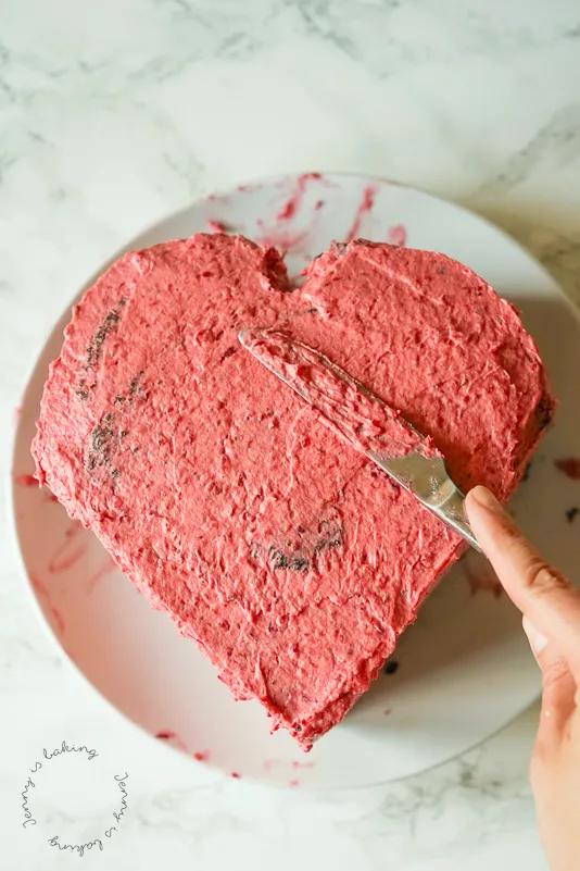 Nahaufnahme einer Herztorte, bei der die oberste Schicht Buttercreme aufgetragen wird, um die Form zu perfektionieren
