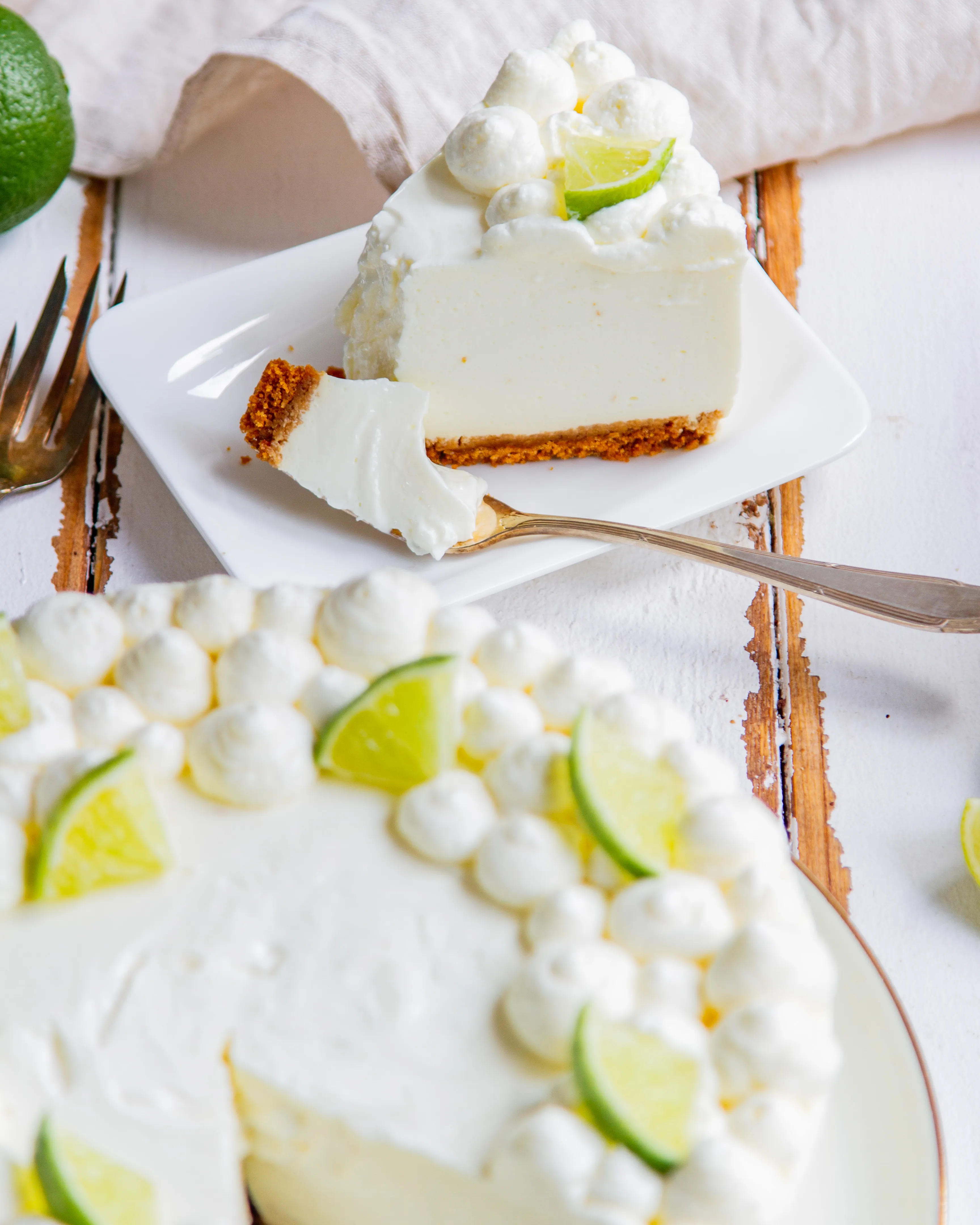 Nahaufnahme einer Limetten-Joghurt-Torte mit Sahnetupfen und Limettenspalten als Dekoration