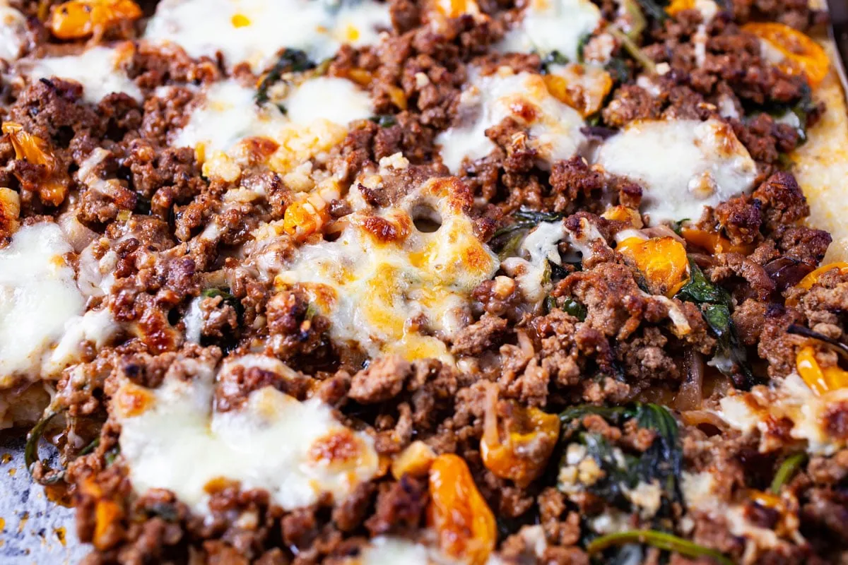 Nahaufnahme einer Pizza mit käsigen Fleischbelägen und Gemüse