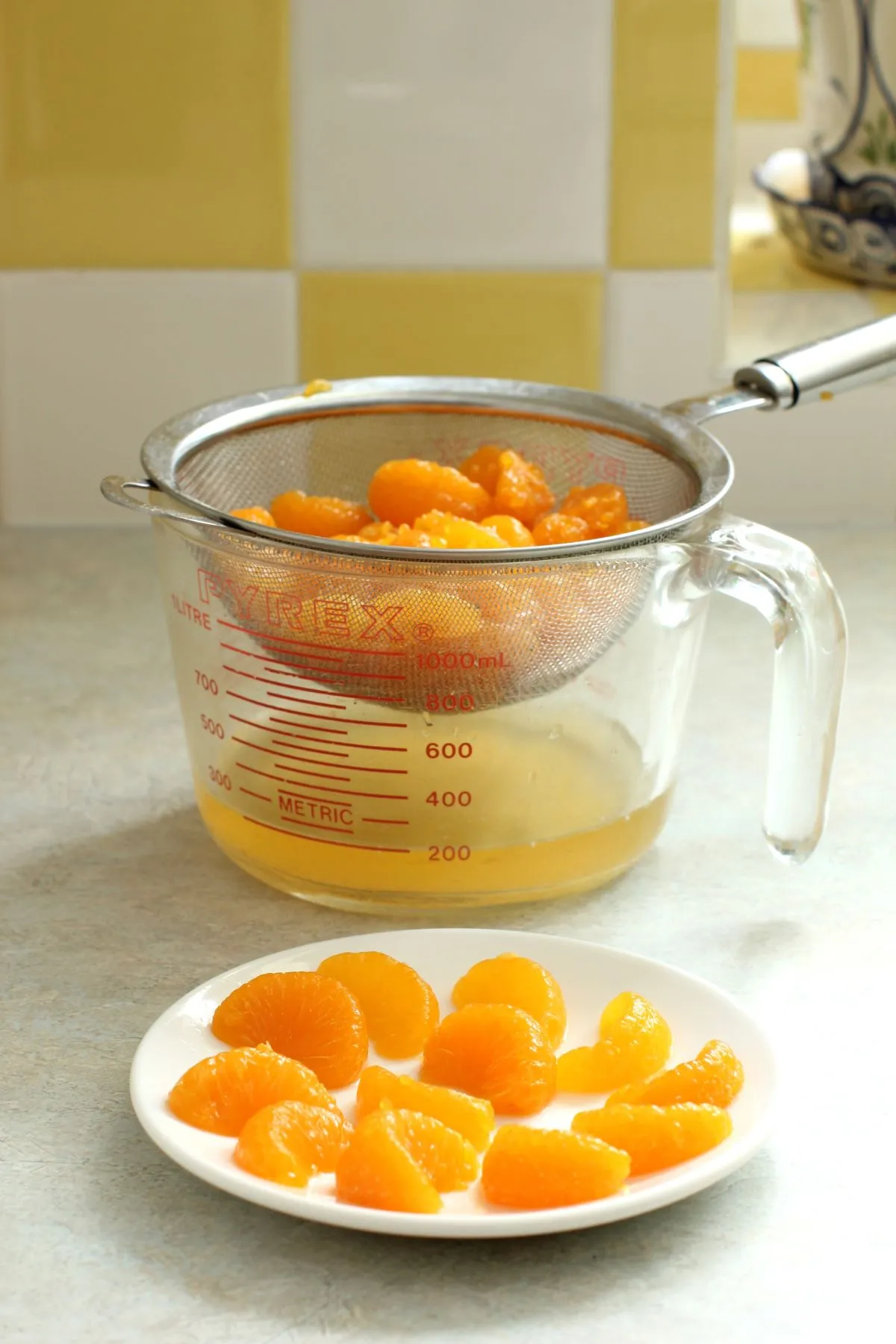 Orangensegmente in einem Sieb über einem Messbecher. Kleiner Teller mit Orangensegmenten davor.