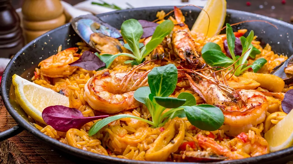 Paella mit Garnelen und einer frischen Salatgarnitur auf einer großen Platte