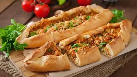 Pide mit Hackfleisch und Käse auf einem Holzbrett, frisch aus dem Ofen