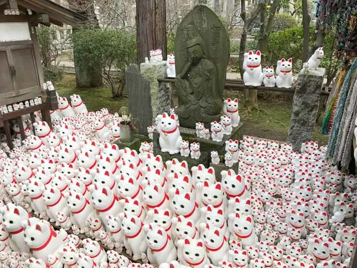 Reihen von kleinen und großen Maneki Nekos im Tempel