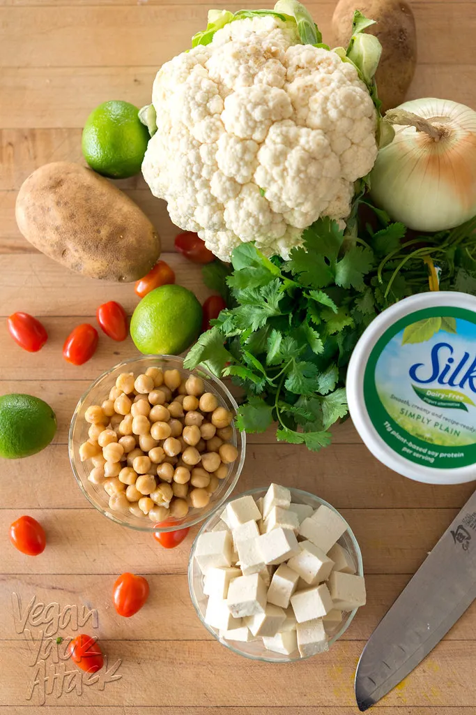 Schüsseln mit Tofu und Kichererbsen, umgeben von Koriander, Gemüse und einem Joghurtbecher