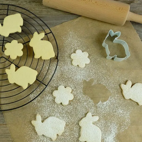 Ungebackene und gebackene Hasenplätzchen auf Backpapier mit Ausstecher