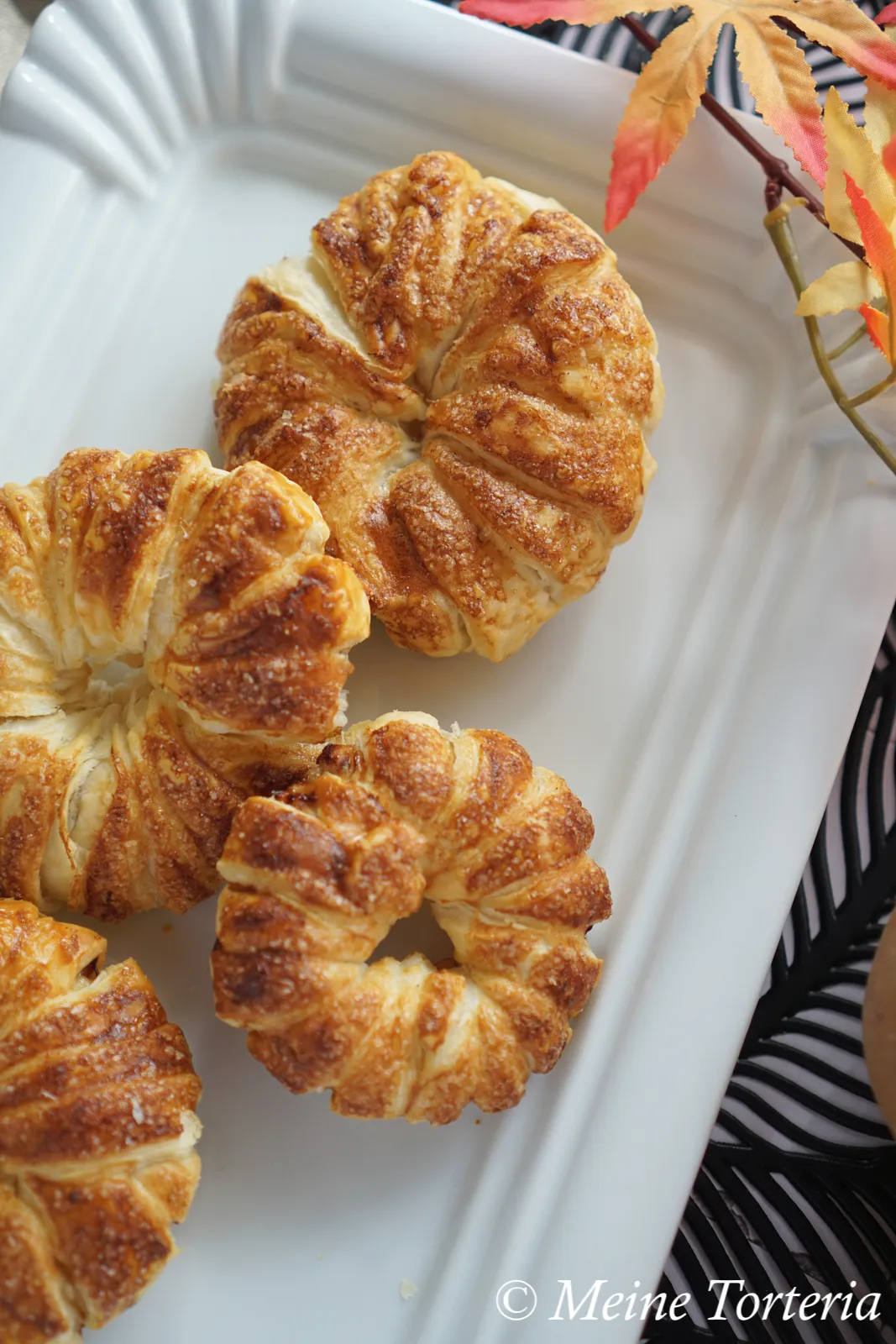 Verschiedene Apfel-Blätterteig-Ringe, teilweise mit Zimtzucker bestreut, auf einem Backpapier