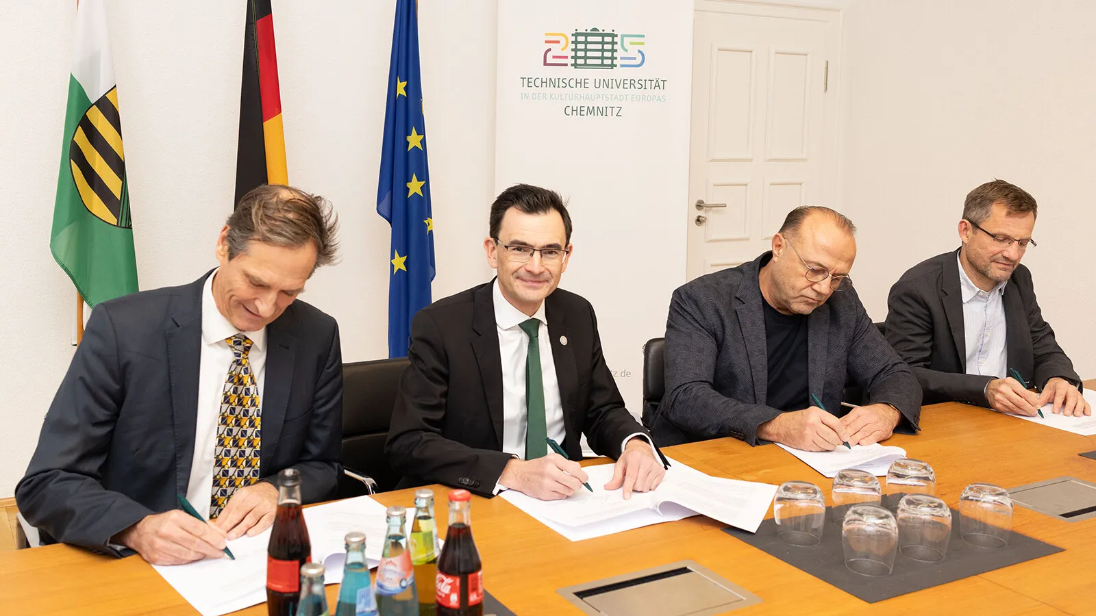 Vier Herren stehen nebeneinander und unterschreiben Dokumente.