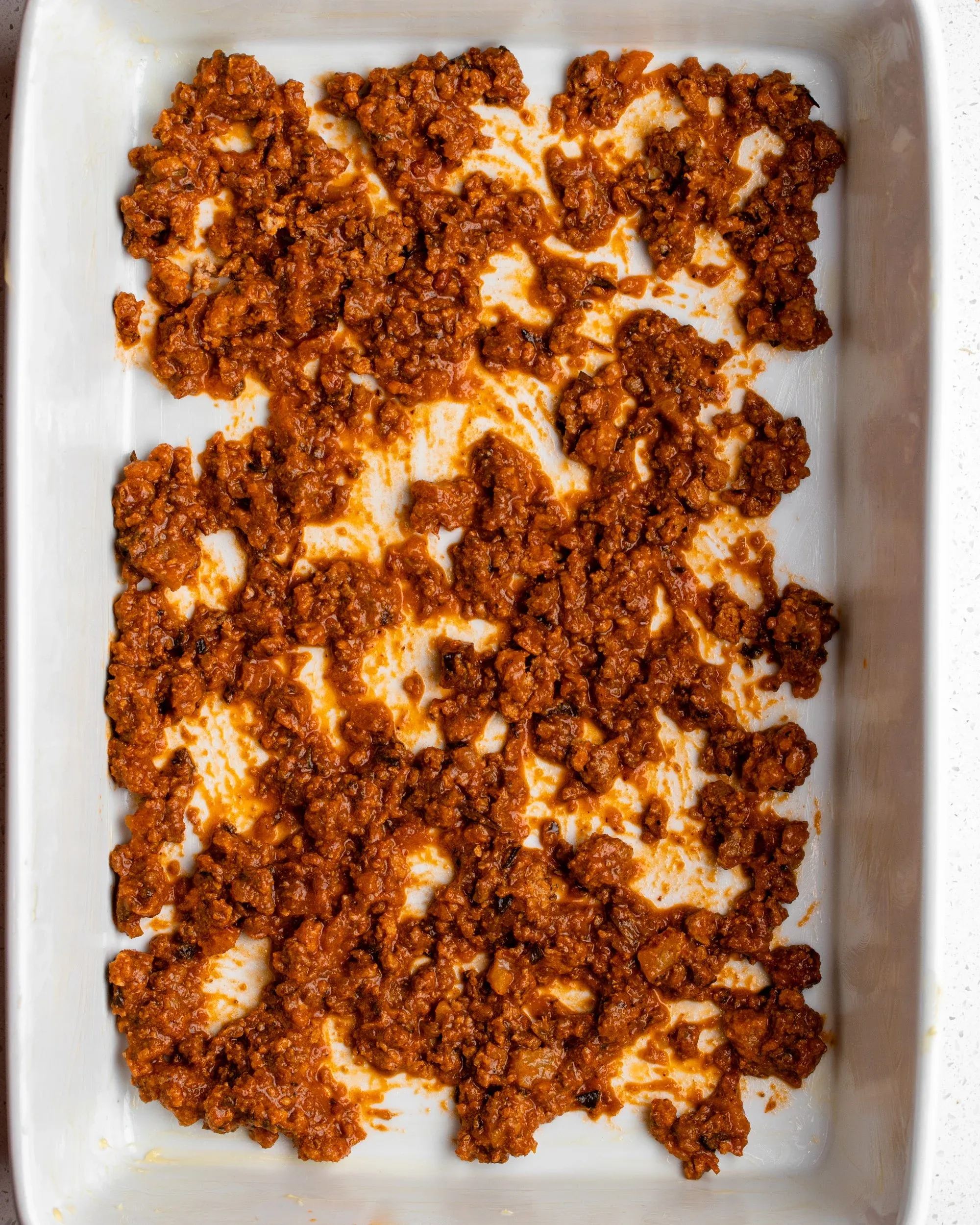 Weiße Auflaufform mit einer Schicht Bolognese am Boden