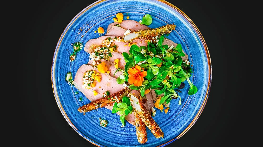 Zarter Kalbstafelspitz mit knusprigem Spargel in Kürbiskernpanier und Ei-Vinaigrette auf einem Teller angerichtet