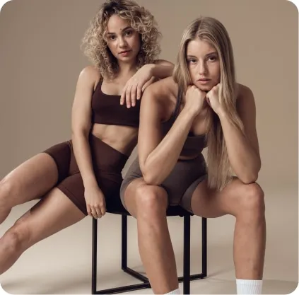 Zwei Frauen in Sportkleidung, die auf einem Stuhl aneinandergelehnt sitzen