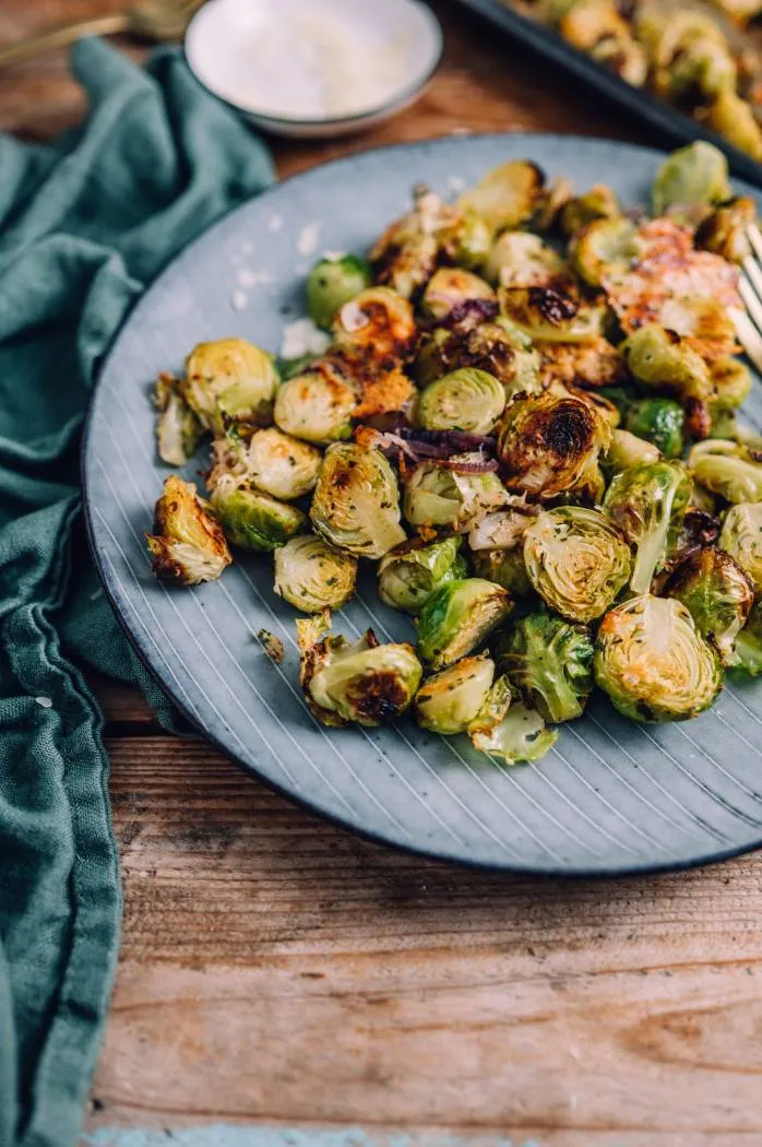 Zwei Hände vermengen Rosenkohl mit Gewürzen