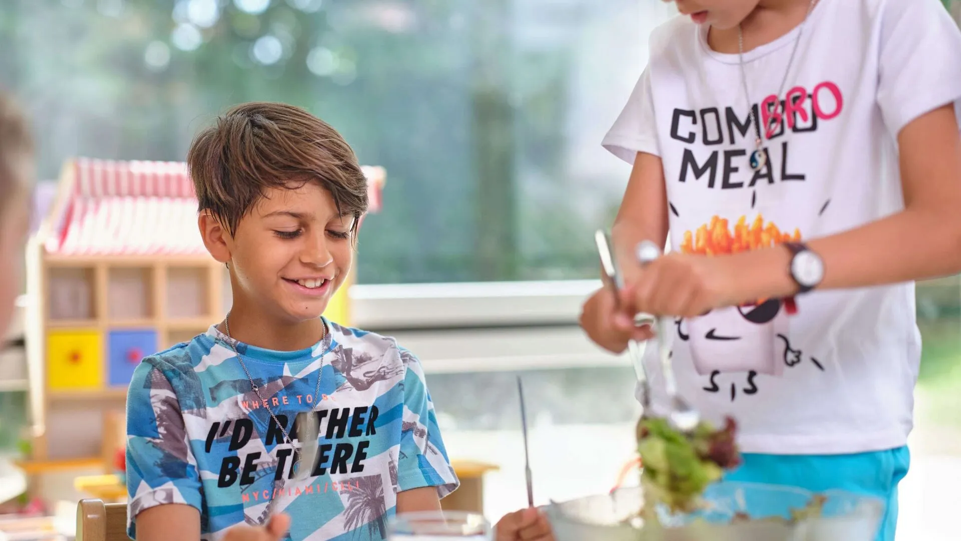 Zwei Knaben in einer Tagesschule, schöpfen Salat und lachen.