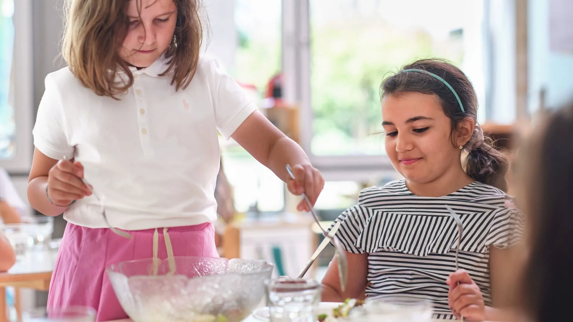 Zwei Mädchen sind in einer Tagesschule, schöpfen Salat und lachen.