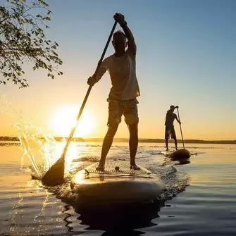 Zwei Männer beim Stand-up-Paddling auf einem See bei Sonnenuntergang – sportliche Aktivität in der Natur